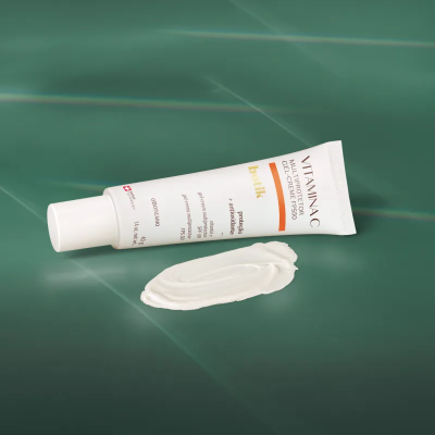 Creme anti-rugas facial vitamina C em tubo branco com tampa, creme espalhado em fundo verde.