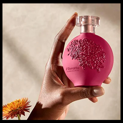 Frasco rosa de perfume Floratta com relevo floral e tampa transparente segurado por uma mão
