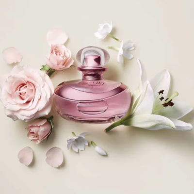 Frasco rosa de perfume com flores rosa e brancas ao redor em fundo claro