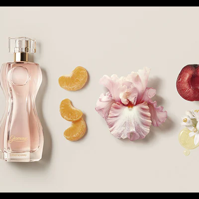 Frasco de perfume rosa com flores e frutas ao lado em fundo claro.