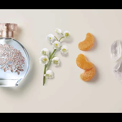 Frasco de perfume com decoração floral, flores brancas, metades de tangerina e pedras de gelo lado a lado