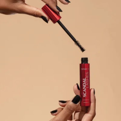 Rímel vermelho com texto SCANDAL LASHES segurado por mãos com unhas pretas