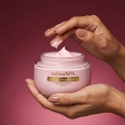 Frasco de creme rosa nativaSPA com mãos femininas segurando e tirando creme