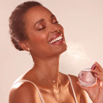 Mulher a segurar frasco de perfume rosa e a sorrir com olhos fechados