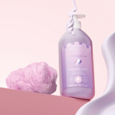 Loção hidratante Algodão Doce em frasco roxo com algodão doce rosa ao lado