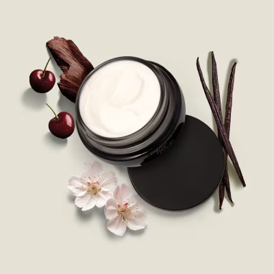 Creme branco em embalagem preta com cerejas, flores brancas, vagens de baunilha e madeira