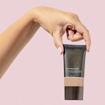 Tubo preto e castanho de base Aqua Hidratante de 30ml segurado por mão feminina