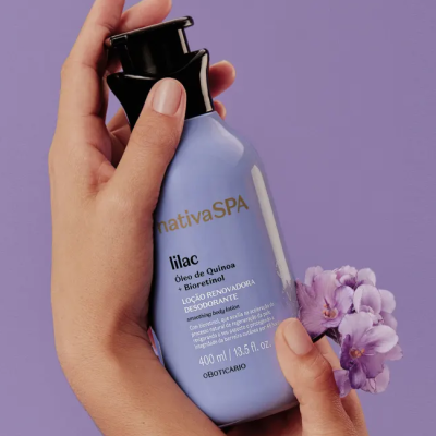 Frasco lilás de loção Nativa SPA com tampa preta segurado por mãos e flores lilás ao lado