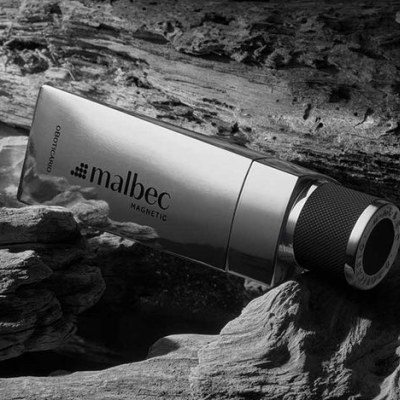 Frasco de perfume Malbec Magnetic prateado entre madeira rústica