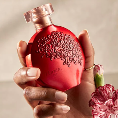 Frasco de perfume vermelho com textura de flores gravadas, mão segurando e flor ao lado