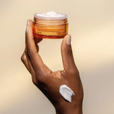 Frasco de creme de vitamina C segurado por mão com creme no dorso