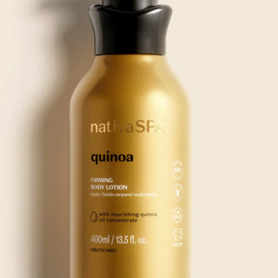 Frasco dourado de loção corporal firmadora quinoa com válvula preta sobre superfície clara