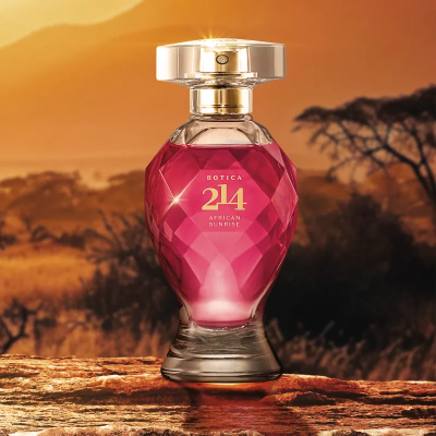 Frasco de perfume rosa e dourado sobre madeira com paisagem de pôr do sol ao fundo