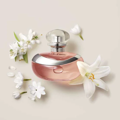 Frasco de perfume rosa com tampa prateada e flores brancas ao redor