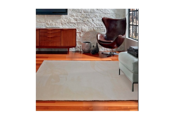 Tapete bege claro sobre chão de madeira em sala com cadeira de couro marrom e móvel de madeira