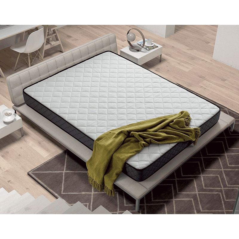 Colchão branco com bordas pretas numa cama cinzenta com manta verde numa sala com chão de madeira e tapete cinzento