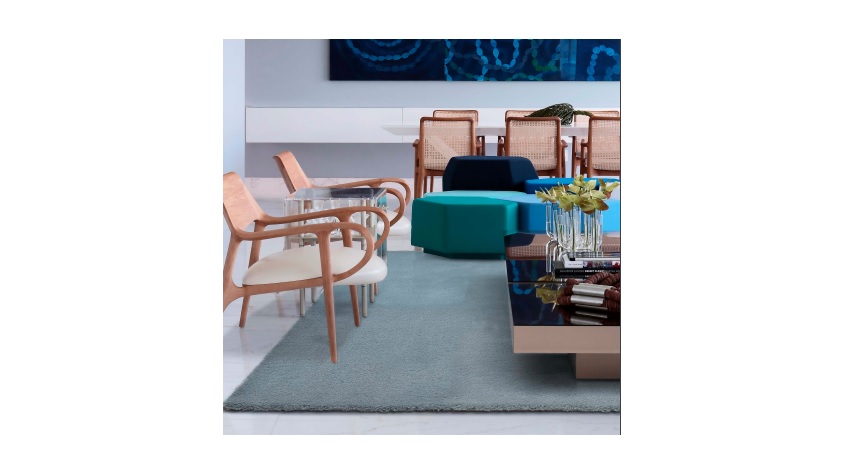 Sala de estar com cadeiras de madeira clara, sofá azul escuro, mesa de centro azul e turquesa, e tapete cinza claro