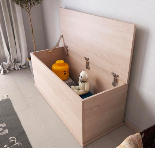 Baú de madeira clara aberto com brinquedos, numa divisão com cortinas e tapete cinzento