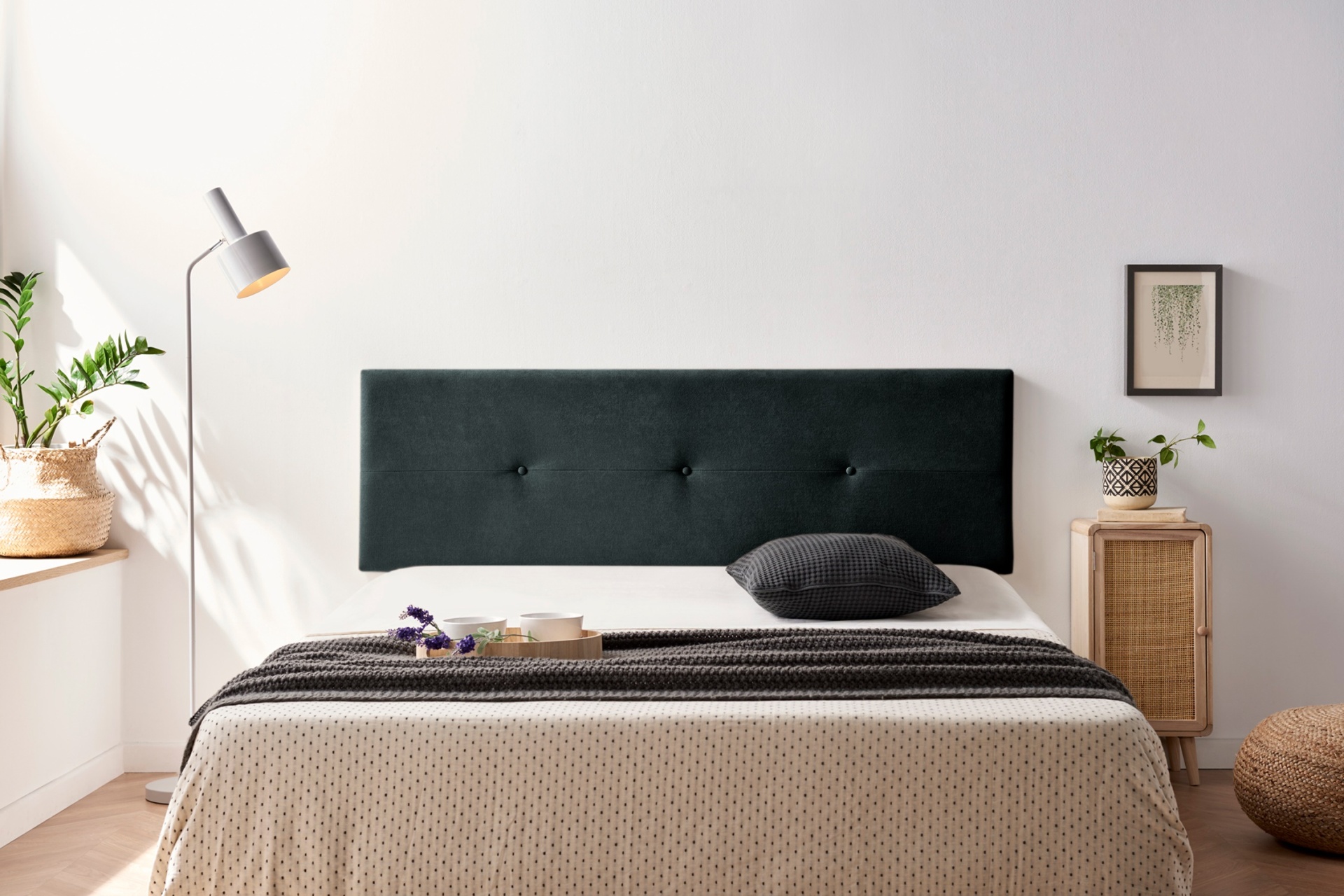 Quarto com cama de cabeceira preta, roupa de cama bege e cinzento, candeeiro branco e plantas