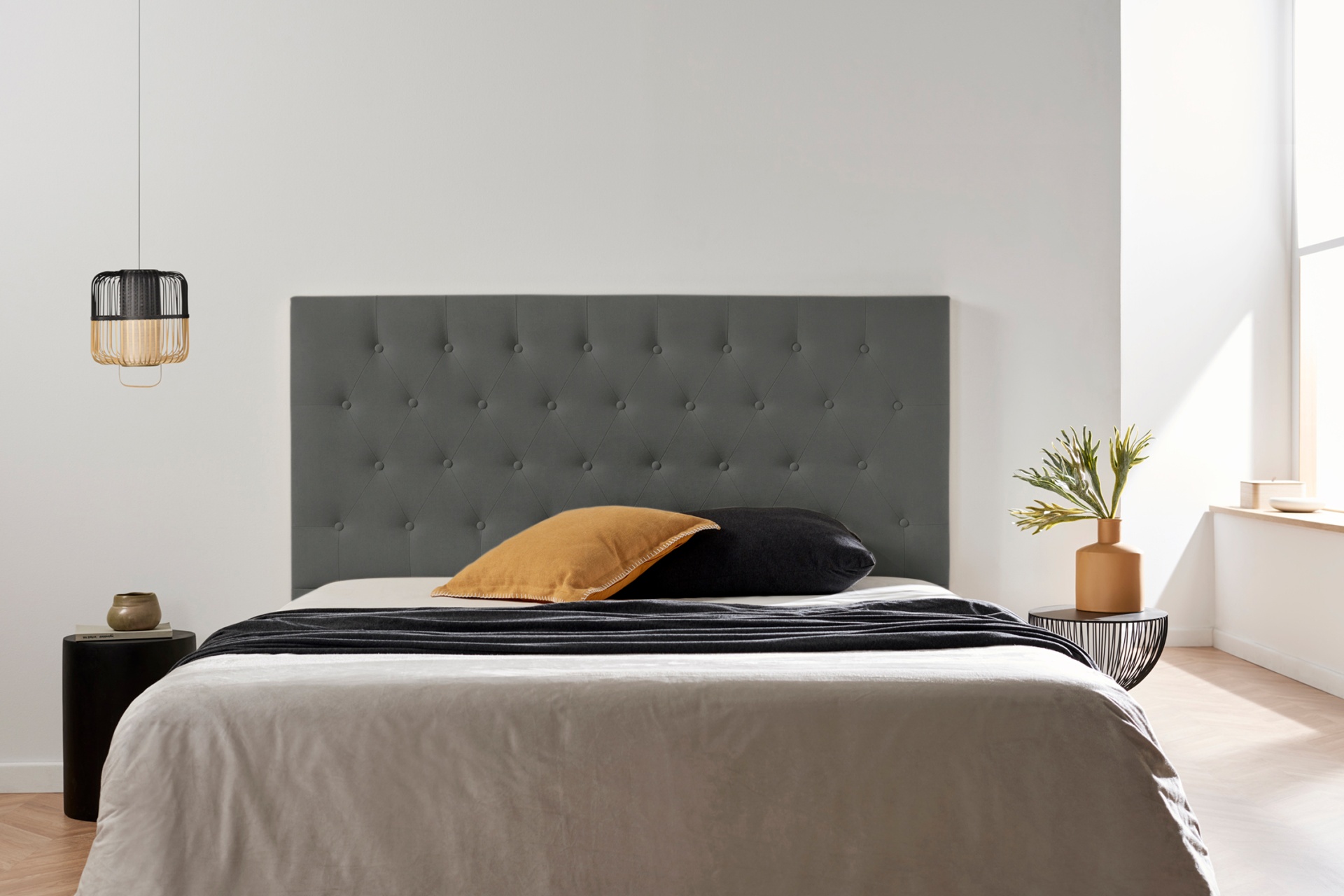 Cama com cabeceira estofada cinzenta e roupa de cama neutra num quarto minimalista