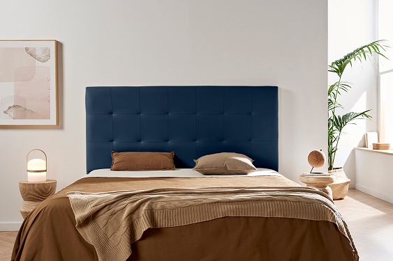 Cama com cabeceira azul, roupas castanhas, mesas de cabeceira de madeira, quadro e planta