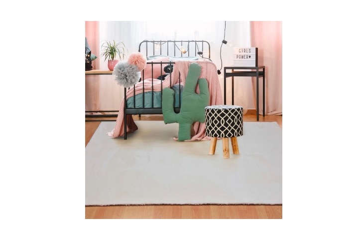 Quarto com cama de ferro, almofadas decorativas, puff e tapete claro