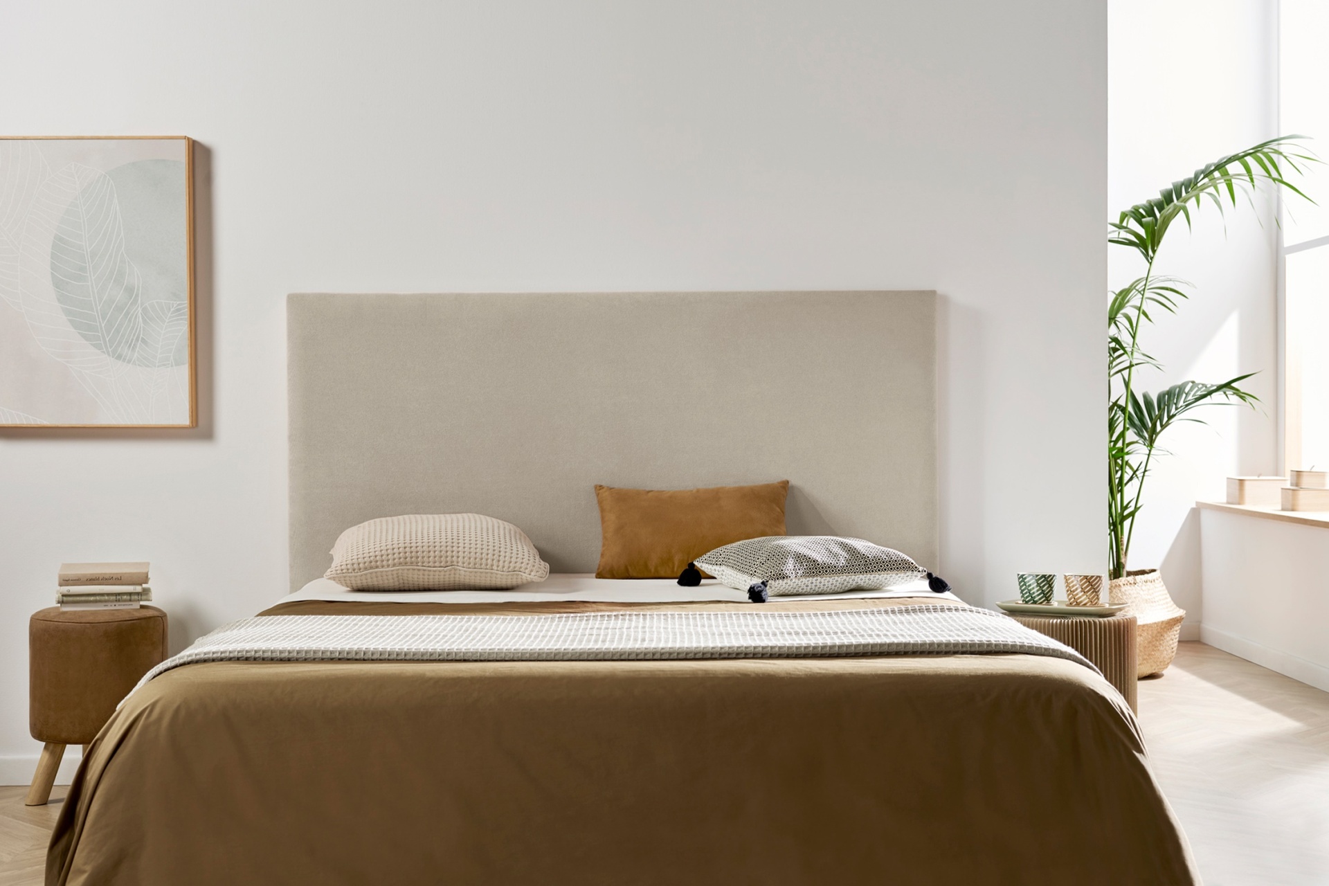 Cama estofada bege com roupa de cama castanha e almofadas decorativas em quarto claro