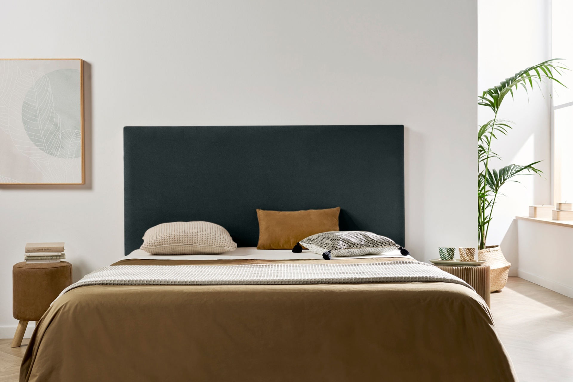 Quarto com cama, cabeceira preta, almofadas bege e castanho, parede branca, mesa de cabeceira e planta