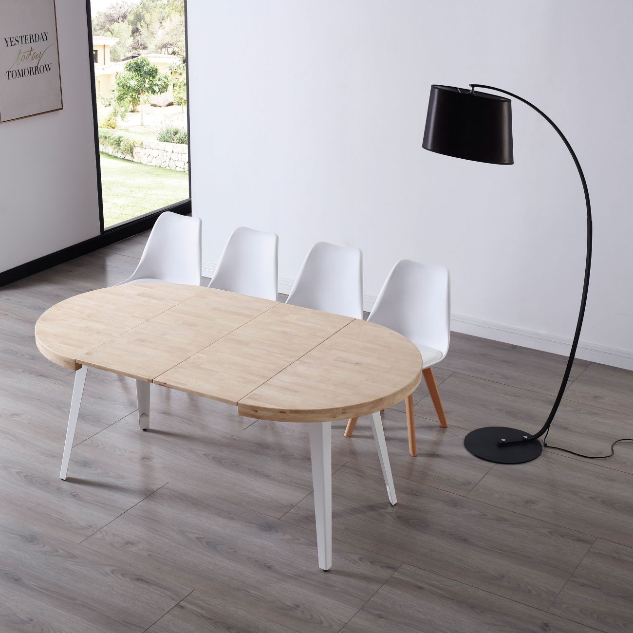 Mesa de madeira clara oval com cadeiras brancas e candeeiro de pé preto num ambiente interior