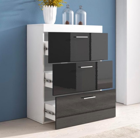 Cômoda branca com gavetas pretas brilhantes, vaso branco com flores amarelas e frascos de vidro sobre a cômoda