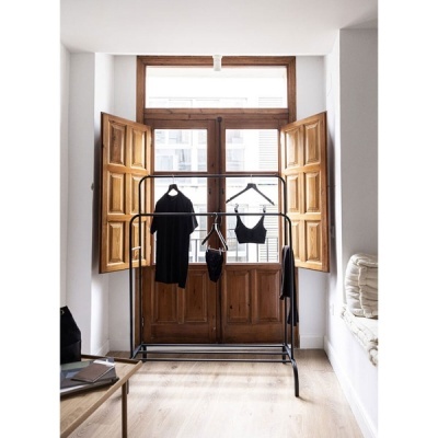 Cabideiro preto com roupas pretas diante de porta de madeira e janelas abertas