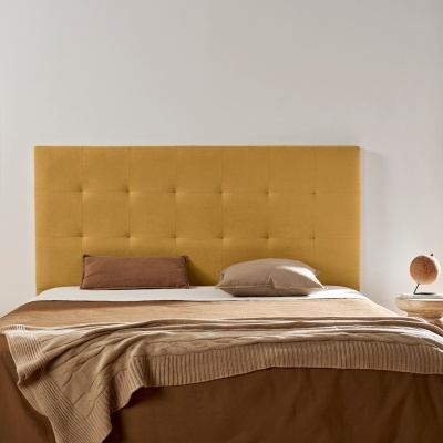 Quarto com cama de casal e cabeceira amarelo mostarda, duas mesas de cabeceira em madeira clara, candeeiro e planta verde junto à janela.