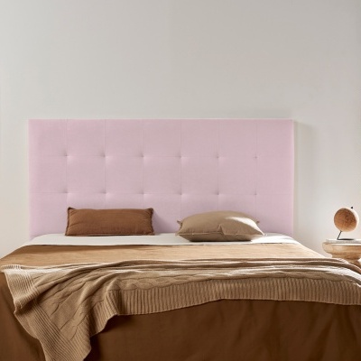 Cama com cabeceira rosa clara estofada, roupa de cama castanha e bege, mesa de cabeceira com candeeiro, quadro abstrato e planta junto a janela