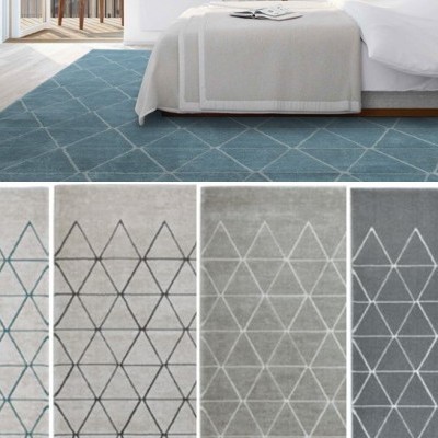 Tapete moderno com padrão de triângulos em quatro cores diferentes em ambiente de quarto com cama branca.