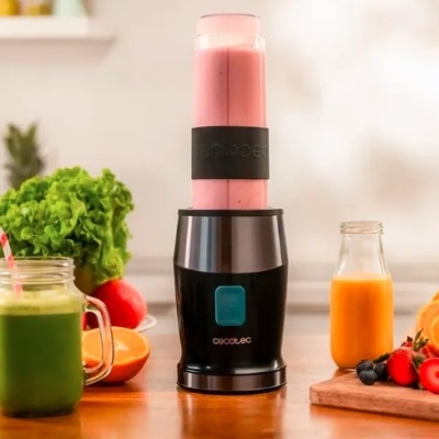 Liquidificador portátil com smoothie rosa numa cozinha com frutas e sumos