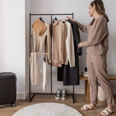 mulher a segurar casaco num cabideiro com roupa neutra e mala preta ao lado