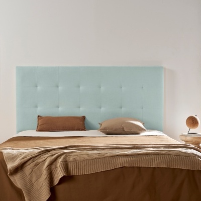 Cabeceira de cama azul claro estofada, cama com roupa e almofadas castanhas, mesas de cabeceira de madeira, quadro pastel e planta verde