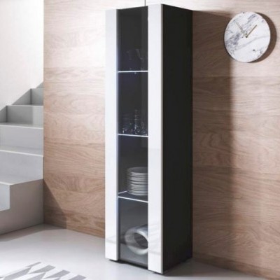 Móvel alto estreito em preto e branco com portas de vidro, com pratos e copos, junto a parede de madeira e relógio marmoreado.