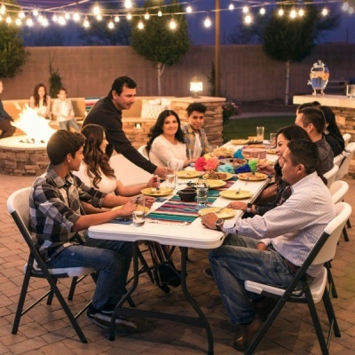 mesa dobrável branca com comida e cadeiras dobráveis ao ar livre com luzes e lareira