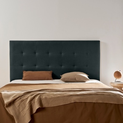 Cama com cabeceira verde escuro, roupa de cama castanha e bege, mesa lateral com abajur, quadro na parede, planta perto da janela