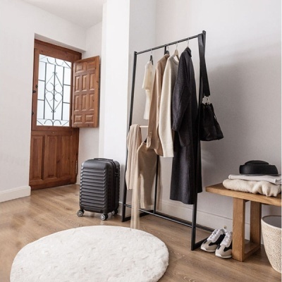 Roupas penduradas em cabide preto, mala preta de rodinhas, tapete branco redondo e ténis num quarto minimalista