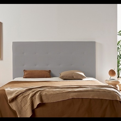 Cama com cabeceira cinzenta, roupa de cama marron e bege, mesa de cabeceira com candeeiro e planta