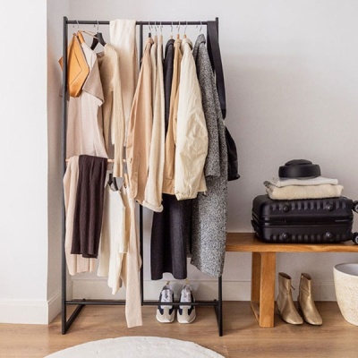 Arara de roupas com casacos e calças em tons neutros ao lado de mala e botas