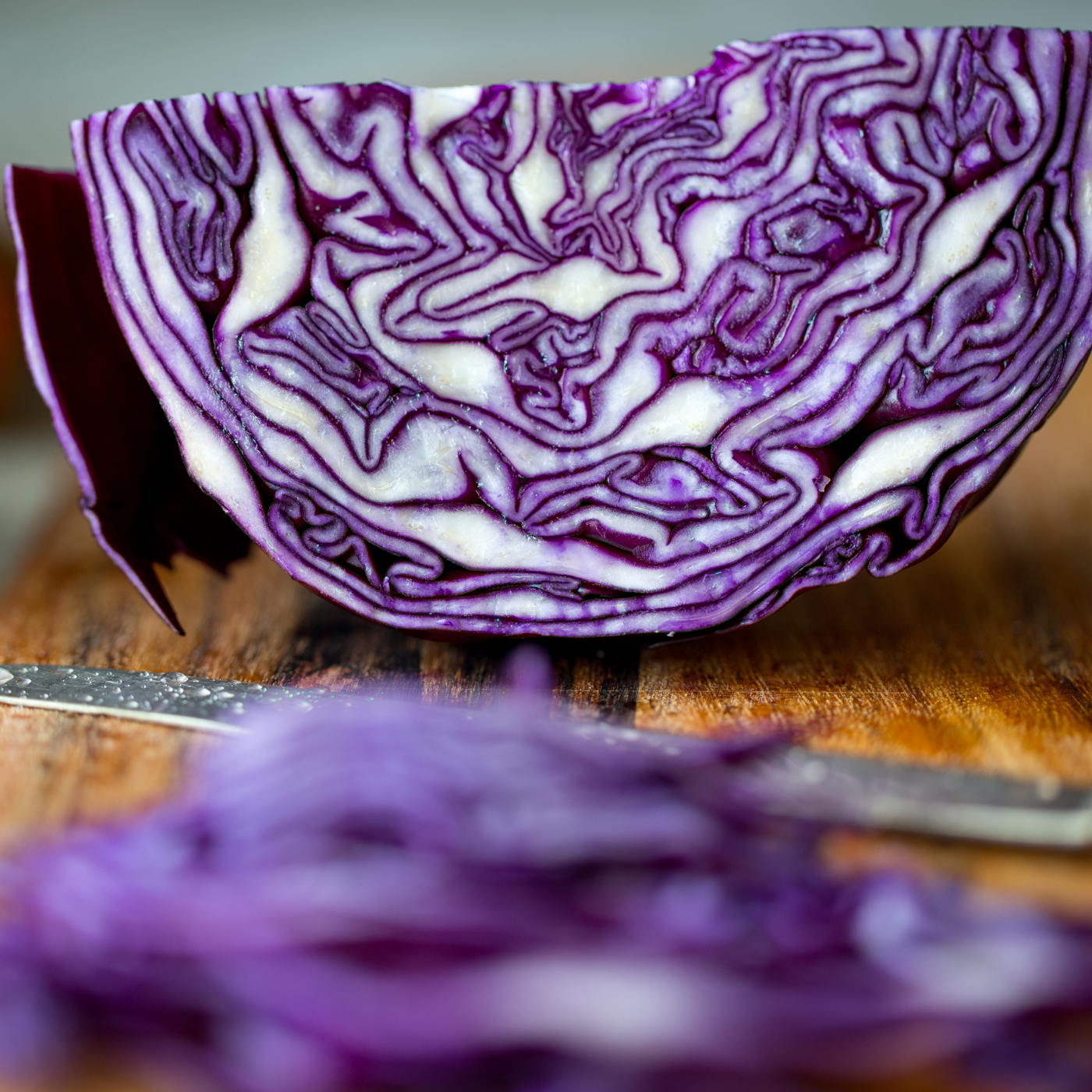 Meia cabeça de couve roxa cortada sobre tábua de madeira com faca ao fundo