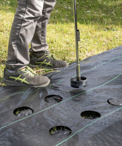 Tecido agrícola preto com orifícios e ferramenta de plantação num jardim