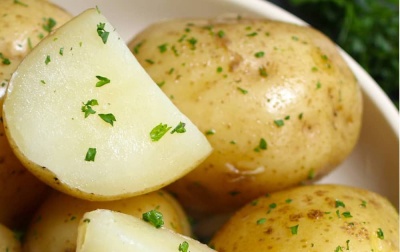 Batatas pequenas amarelas cortadas ao meio num recipiente branco com ervas verdes