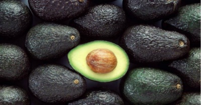 Abacates com casca rugosa, um cortado ao meio mostrando polpa e caroço