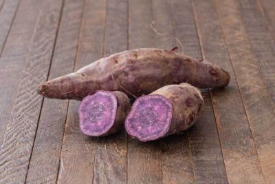 Batata-doce roxa cortada e inteira sobre madeira escura