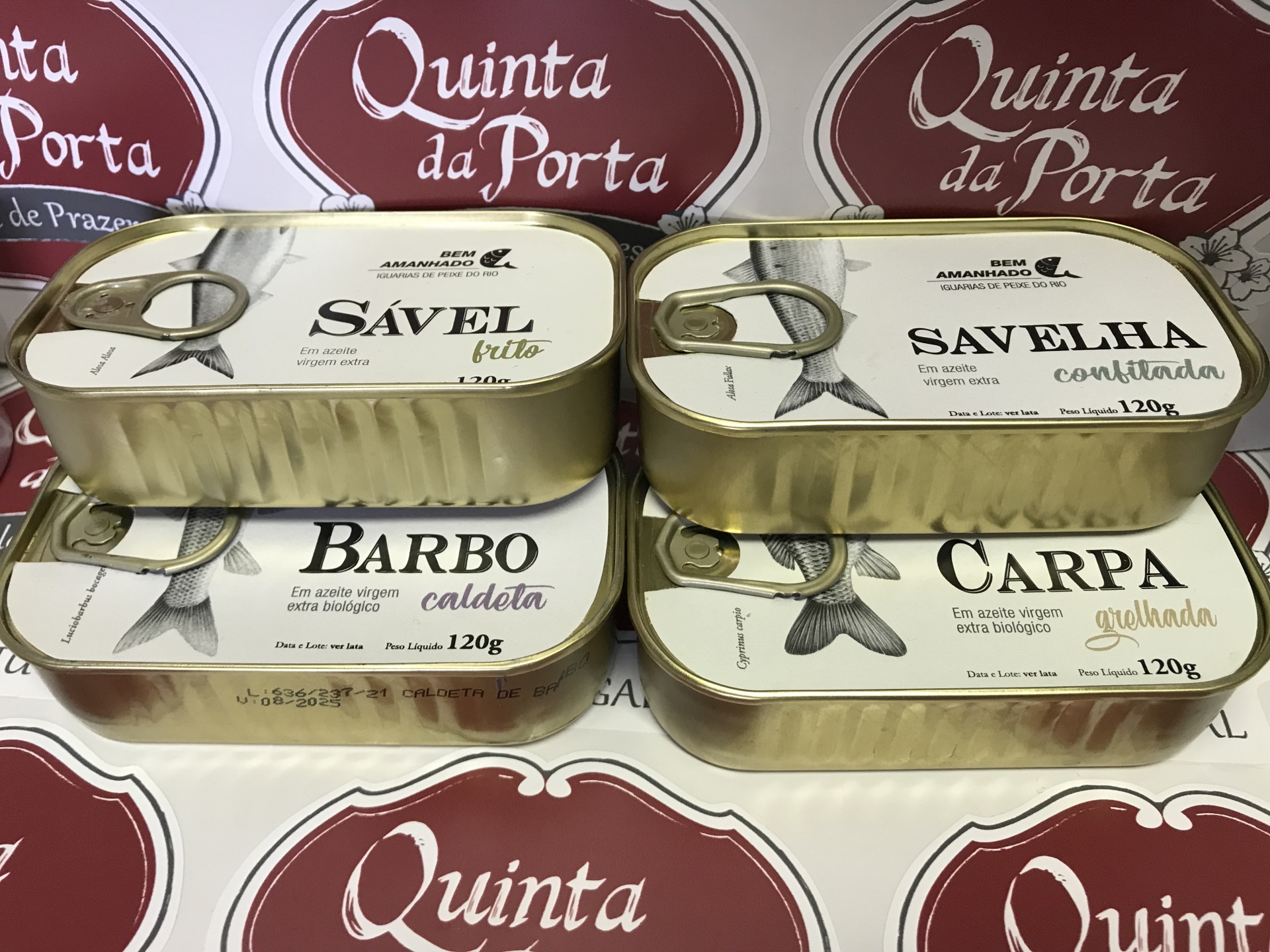 Truta abafada Quatro latas de conservas de peixe com rótulos brancos e texto preto sobre padrão vermelho e branco Quinta da Porta