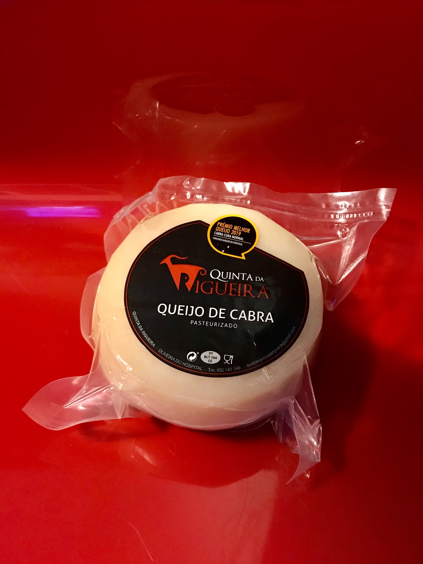 Queijo de Cabra - Quinta da Rigueira Queijo de cabra embalado a vácuo com rótulo preto sobre fundo vermelho